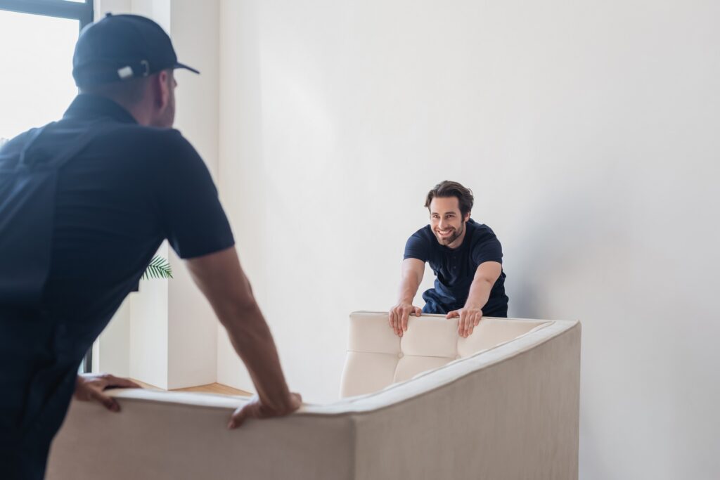 smiling worker moving white sofa with blurred colleague